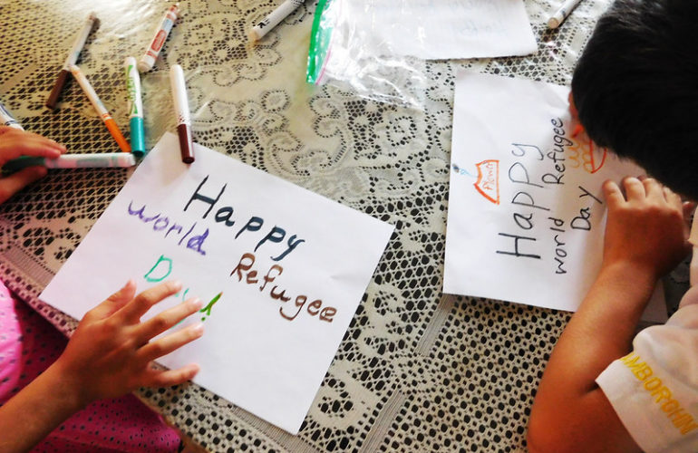 Photo showing two resettled children in the U.S. drawing illustrations for World Refugee Day